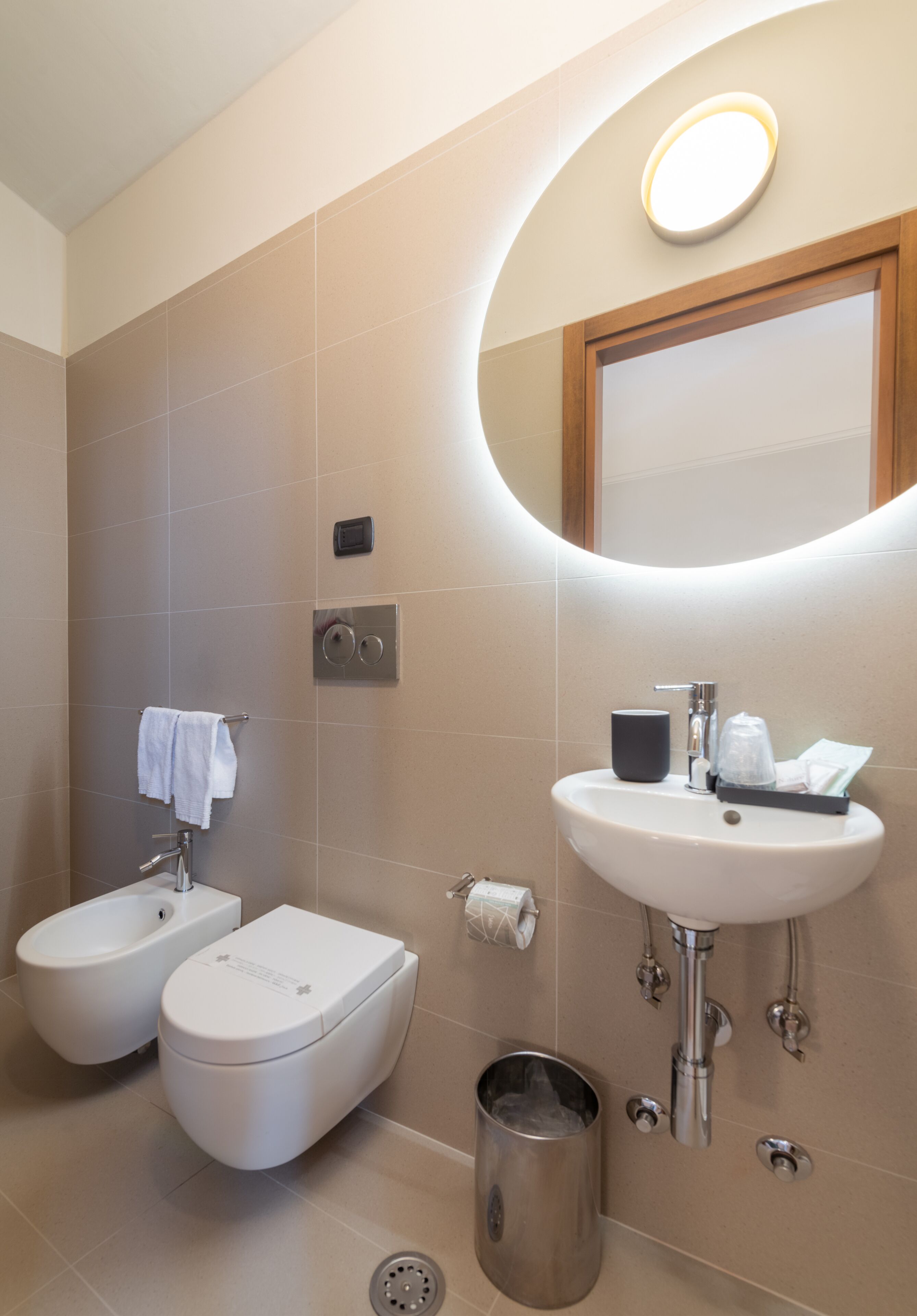 A modern bathroom with a bidet, toilet, sink, and a mirror with a light above it.