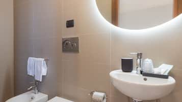 Ein modernes Badezimmer mit einer Bidet, Toilette, Waschbecken und einem Spiegel mit Beleuchtung darüber.