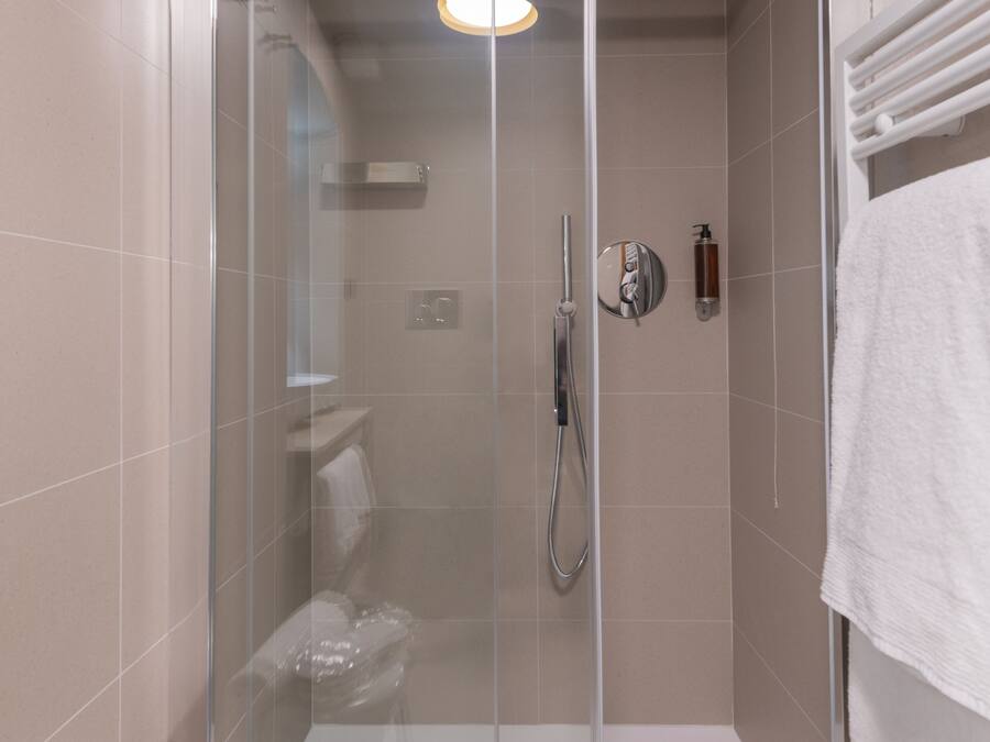 A modern shower enclosure with a glass door, a built-in bench, and a towel rack.