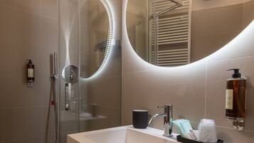 Un baño moderno con ducha de mampara de vidrio, lavamanos blanco y un espejo grande.