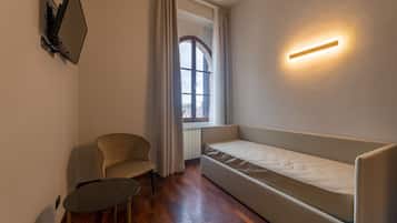 Una stanza compatta con divano letto, un piccolo tavolo rotondo, una sedia e un punto luce a parete.
