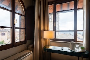 Habitación de hotel con vista a la ciudad, una mesa con una lámpara, un hervidor, y una bandeja con una taza y una tarjeta.