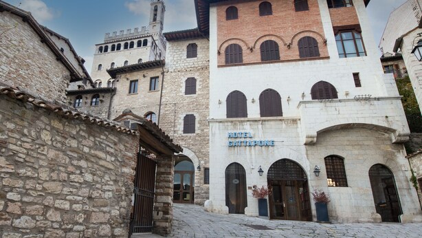 Un edificio histórico con un letrero que dice 'Hotel Gattapone'. Cuenta con paredes de piedra, ventanas de arco y una torre de campanas.