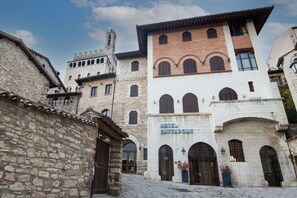 Un edificio histórico con un letrero que dice 'Hotel Gattapone'. Cuenta con paredes de piedra, ventanas de arco y una torre de campanas.