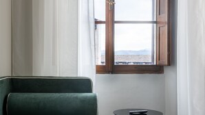 Una habitación con un sofá verde, una mesa redonda pequeña y un ventanal con cortinas.