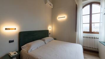 A neatly made bed with white linens, a bedside table with a telephone, and a wall-mounted air conditioner.
