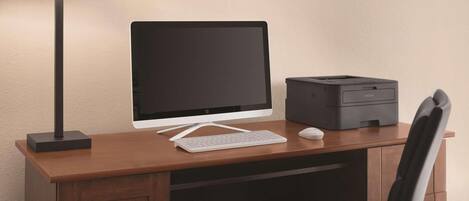 Un escritorio de madera con una computadora de escritorio, una impresora y una lámpara.