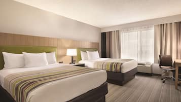Une chambre d’hôtel avec deux lits, un bureau, une chaise, une lampe et une grande fenêtre avec des rideaux.