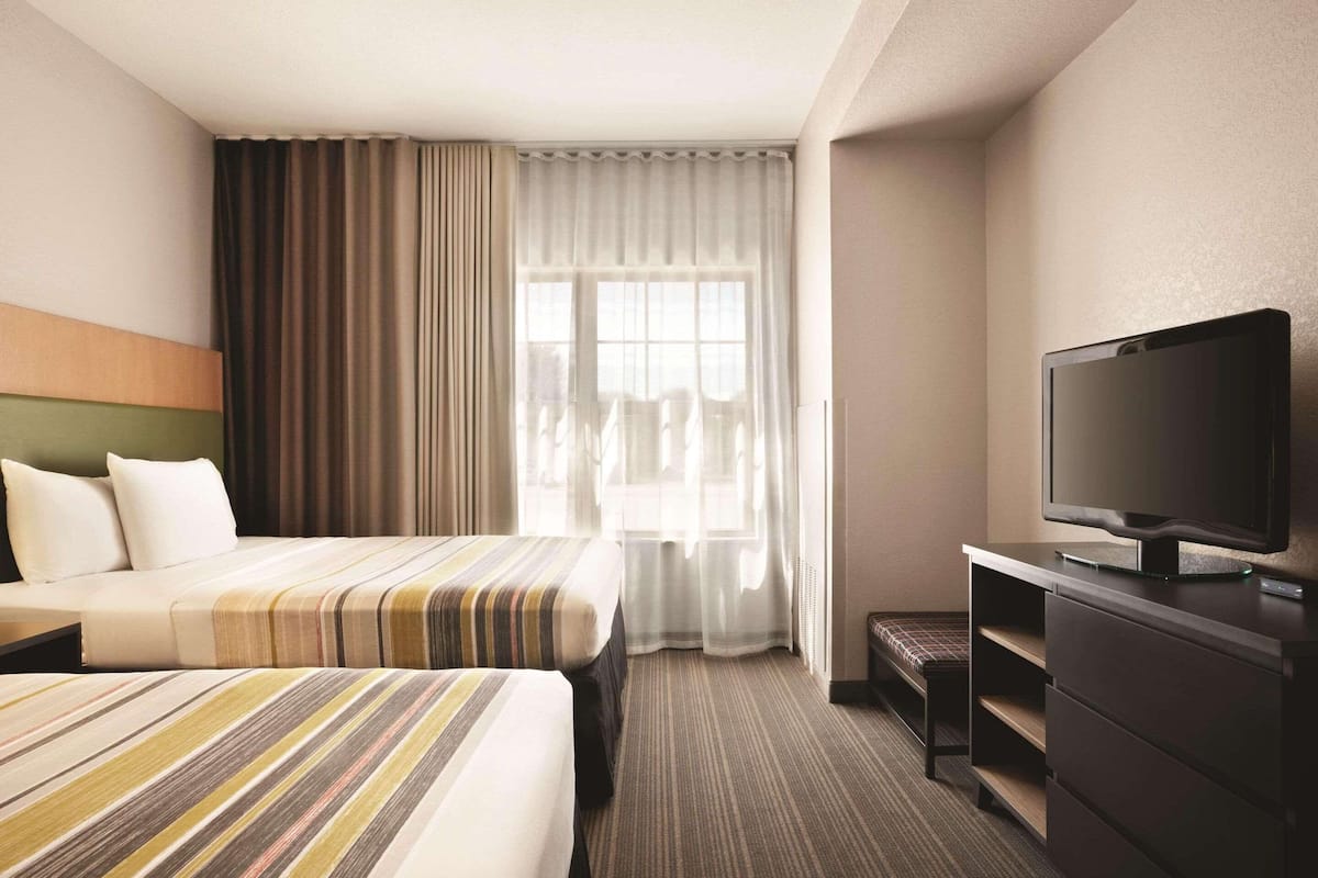 Quarto de hotel com cama, televisão, escrivaninha e janela com cortinas.