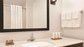 Une salle de bain avec un grand miroir, un lavabo, un porte-serviettes et des articles de toilette posés sur le comptoir.
