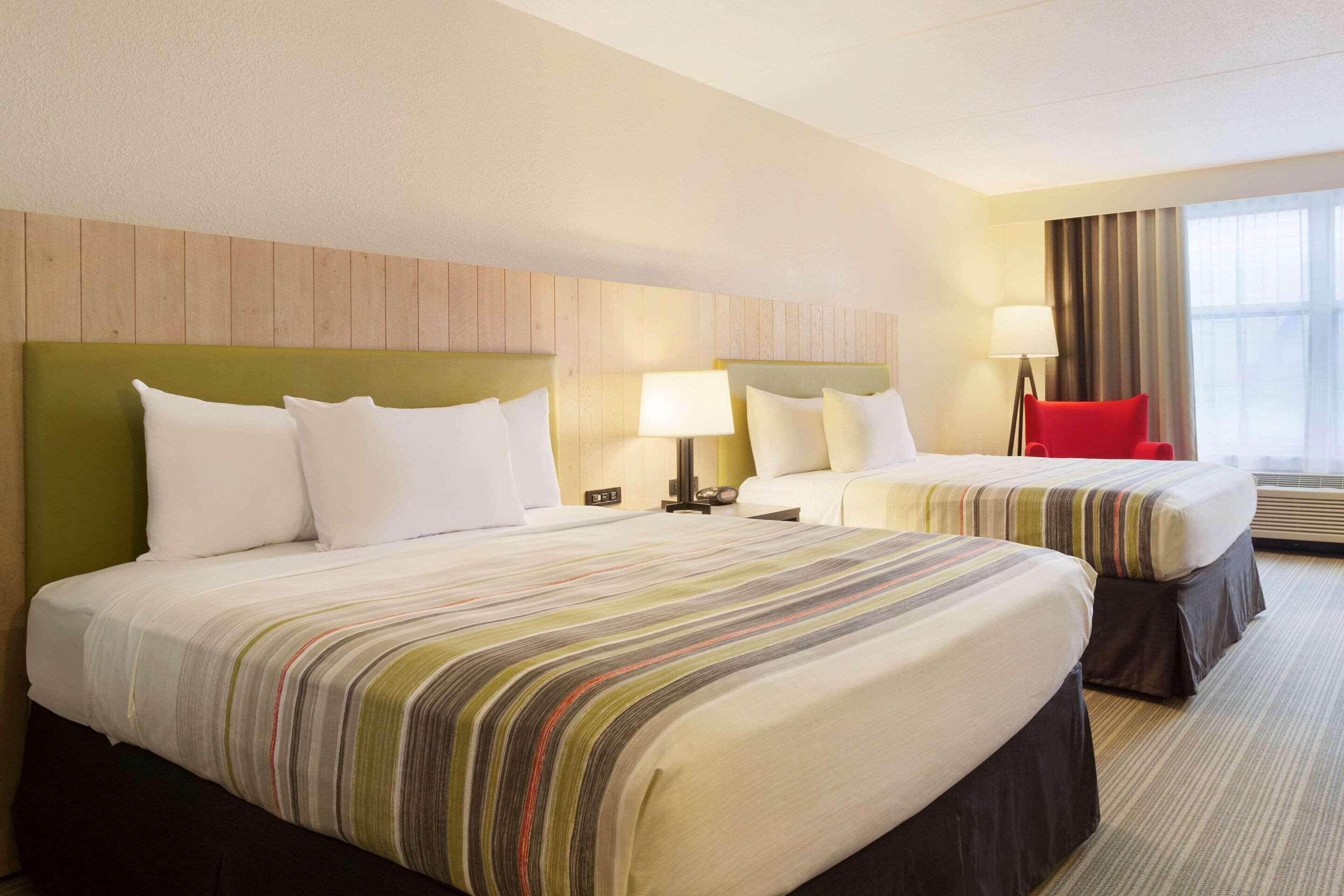 Una camera d'albergo con due letti, una sedia rossa e un'ampia finestra con tende.