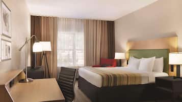 Une chambre d’hôtel comprenant un lit, des tables de chevet, un bureau, une chaise et une fenêtre avec des rideaux.