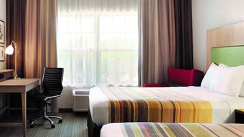 A hotel room with a bed, a desk, a chair, and a window with curtains.