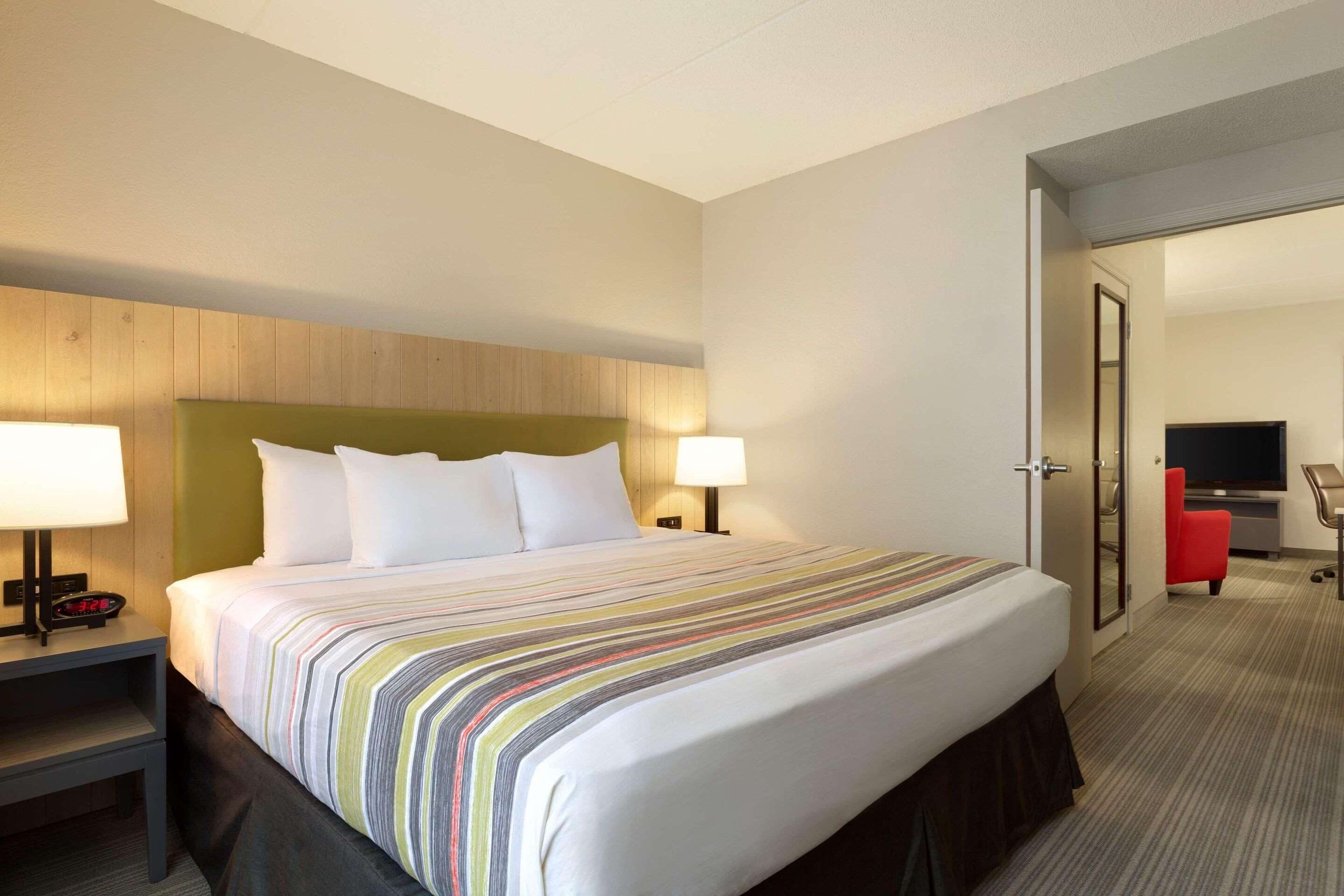 Une chambre d’hôtel avec un grand lit, deux tables de chevet avec des lampes, une télévision et un fauteuil rouge.