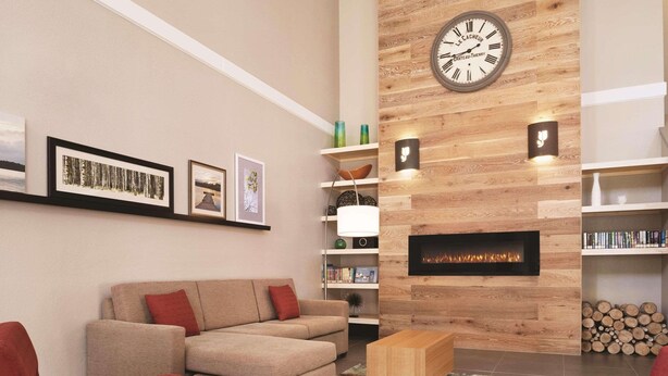 Un salon moderne avec un canapé beige, des fauteuils rouges, un mur décoratif en bois orné d’une horloge et une cheminée.