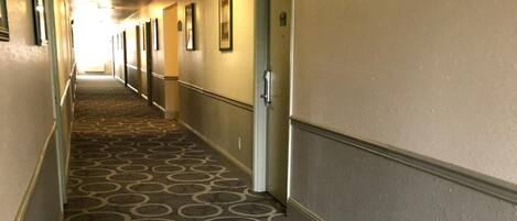 Un pasillo de hotel con alfombra estampada, puertas y cuadros en las paredes.