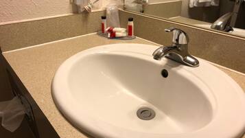 A white bathroom sink with a single faucet, a mirror above it, and toiletries on the countertop.