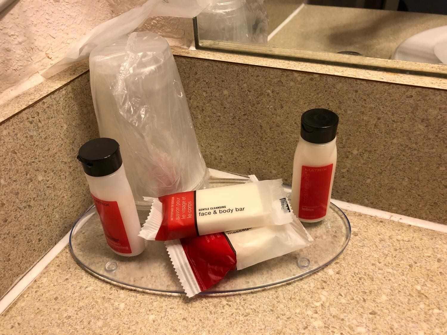 A bathroom counter with toiletries including a face and body bar, a lotion bottle, and a massage bar.