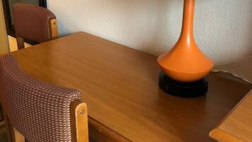 Een houten tafel met een enkele oranje lamp, een gestreept stoel, en een gedeeltelijk zicht op een muur met een ronde decoratie.