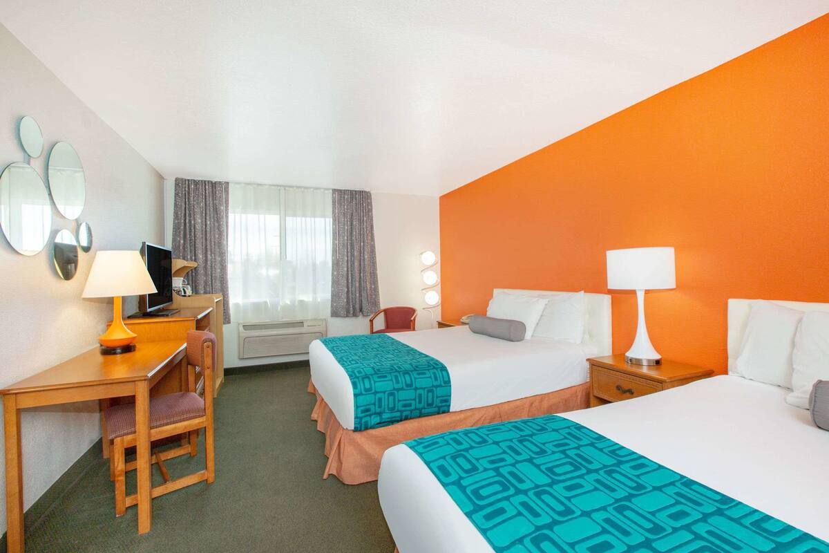 A hotel room with two beds, a desk with a chair, a TV, and a window with curtains.