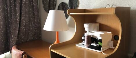 Habitación de hotel compacta con escritorio de madera, una silla, cafetera y lavavajillas.
