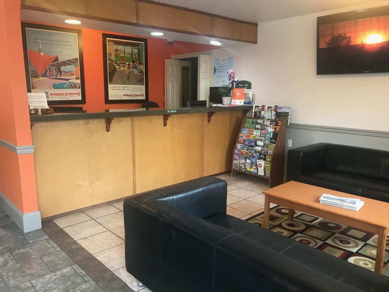 Un'area di accoglienza con un bancone, poster incorniciati, un espositore per riviste, un divano nero e un tavolino da caffè.