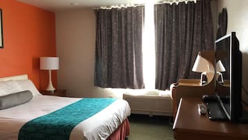 A hotel room with a bed, a desk, a chair, a lamp, a television, and a window with curtains.
