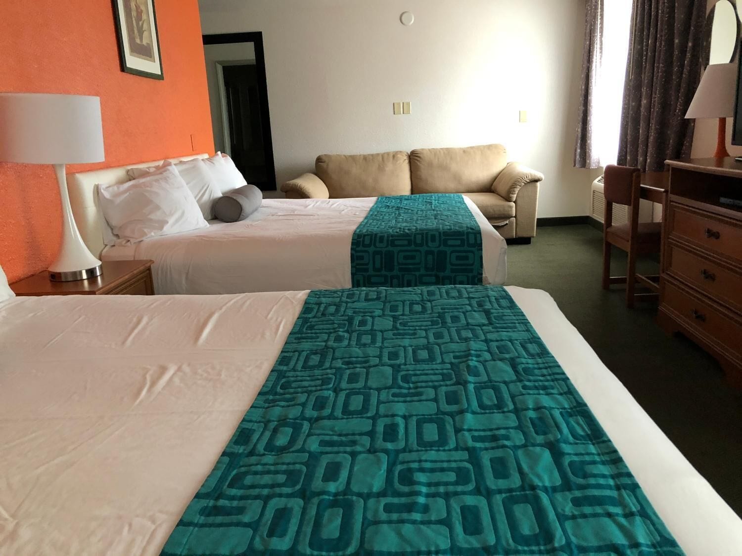 A hotel room with two beds, a sofa, a dresser, and a lamp.