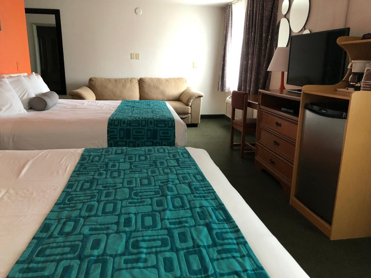 A hotel room with two beds, a sofa, a dresser, a television, and a coffee machine.