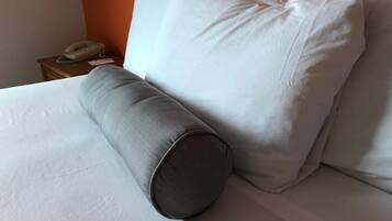 A bed with white bedding, a grey cylindrical pillow, and a white pillow against an orange wall.