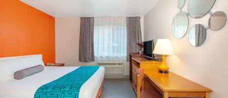 Habitación de hotel con cama, escritorio, silla, lámpara, televisor y una pared con espejos.