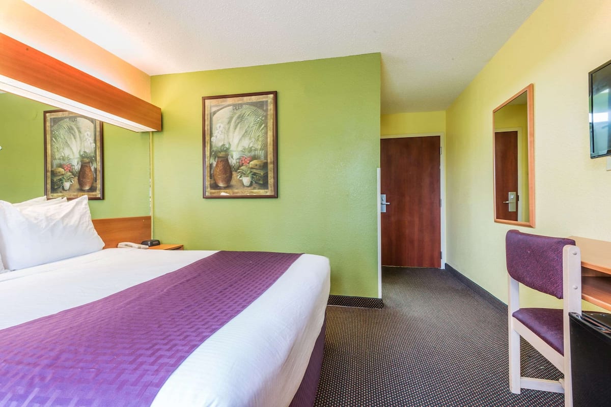A hotel room with a large bed, a desk with a chair, a mirror, and two framed pictures on the wall.