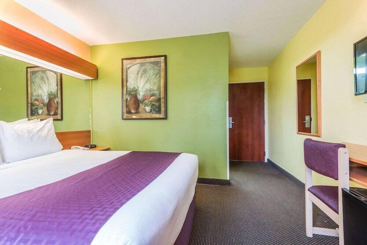 A hotel room with a bed, a desk, a chair, a mirror, and two framed pictures on the wall.