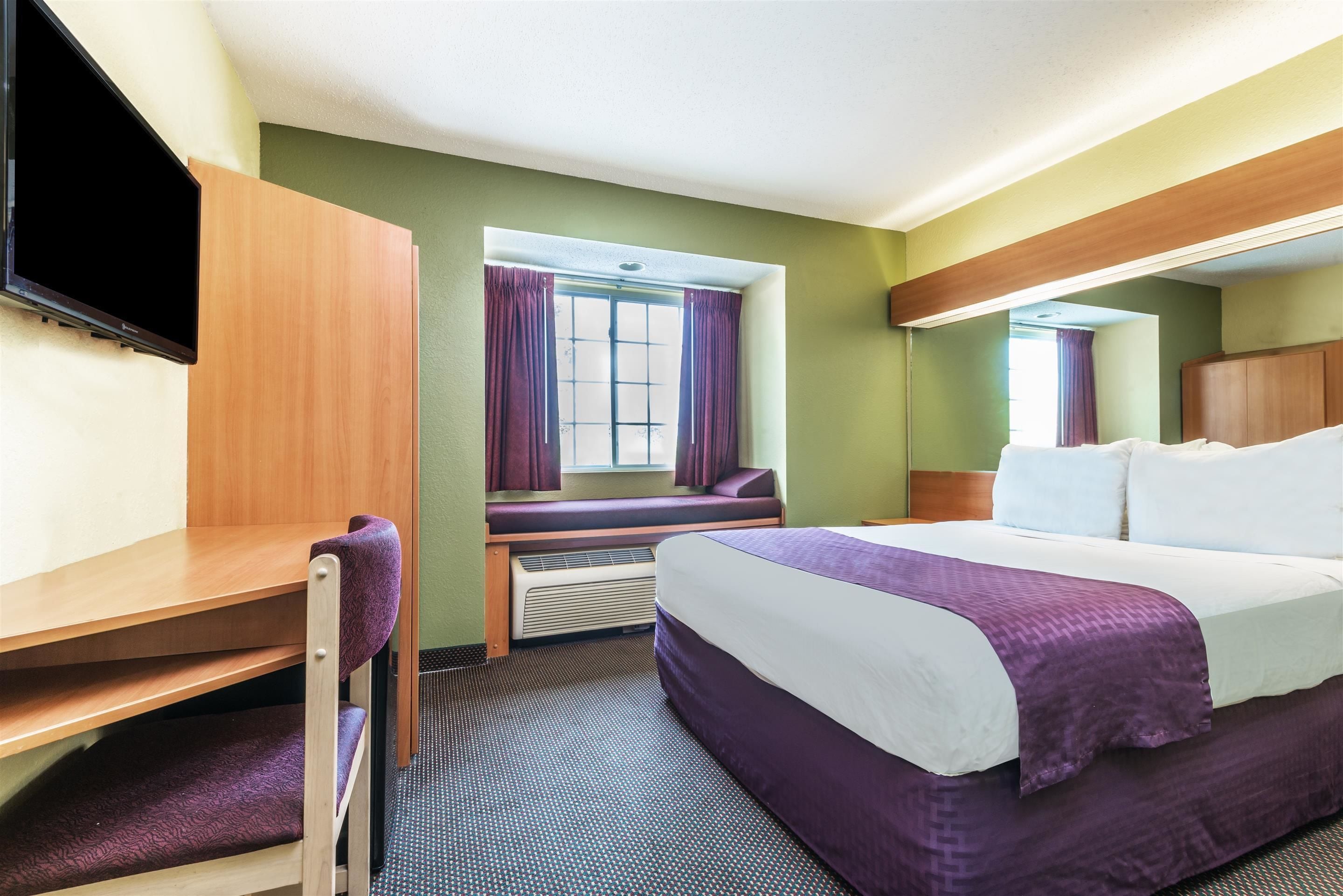 A hotel room with a bed, a desk, a chair, a television, and a window with curtains.