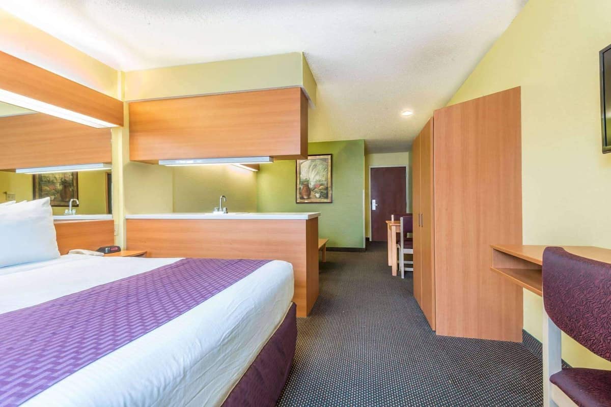 A hotel room with a bed, a desk, a chair, a sink, and a door leading to another room.