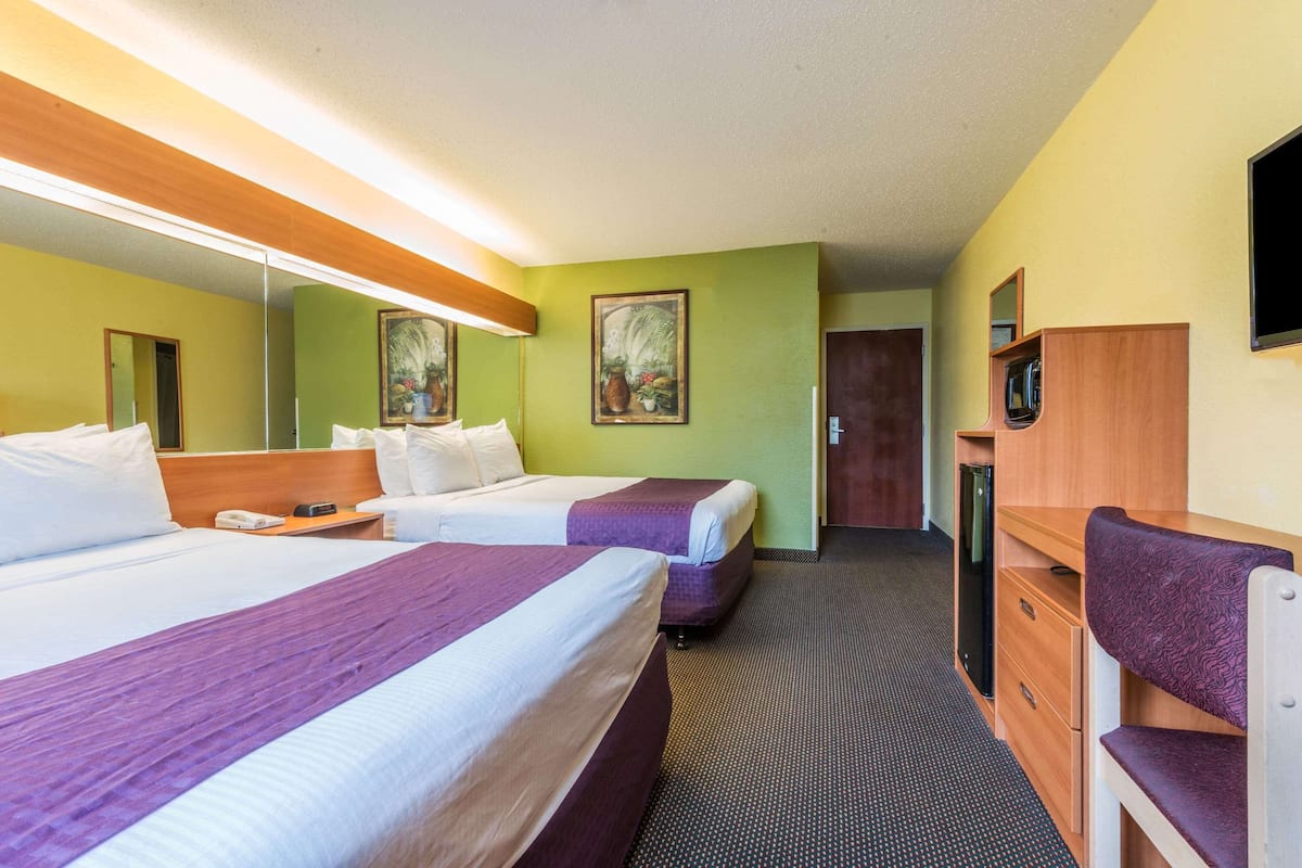 A hotel room with two beds, a desk, a chair, a mirror, and a door.