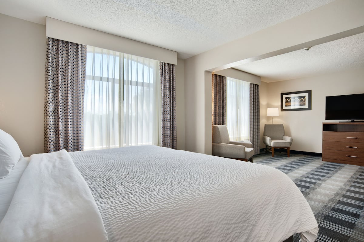 A hotel room with a large bed, a desk, a chair, a television, and a window with curtains.