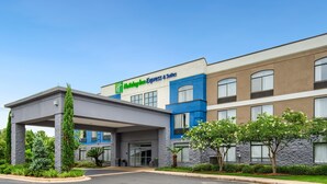 A Holiday Inn Express & Suites building with a covered entrance, stone pillars, and a landscaped front yard.