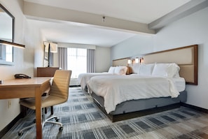 Habitación de hotel con escritorio, dos camas, una silla y un ventanal grande.