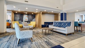 A modern hotel lobby with seating areas, a reception desk, and a large abstract wall mural.
