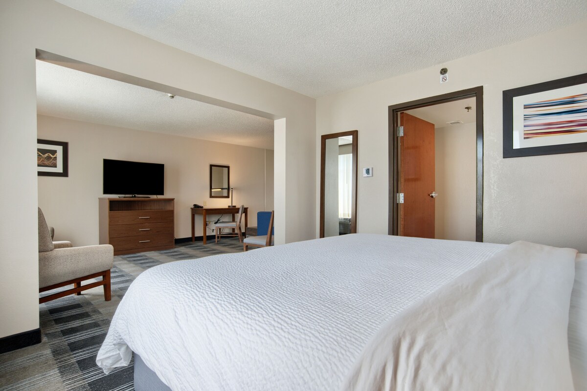 A hotel room with a large bed, a desk with a chair, a television, and a wardrobe.