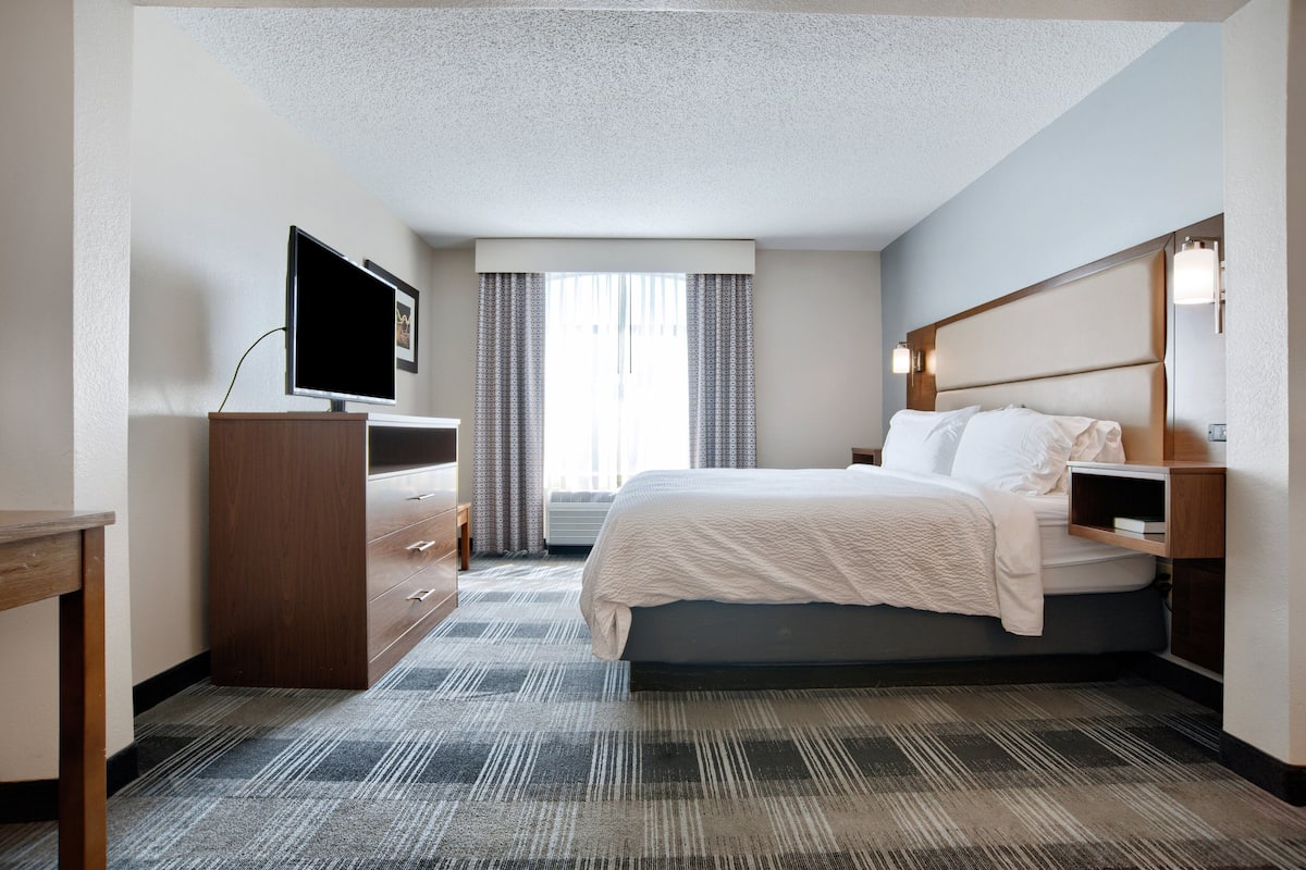 A hotel room with a bed, a TV, a desk, and a window with curtains.