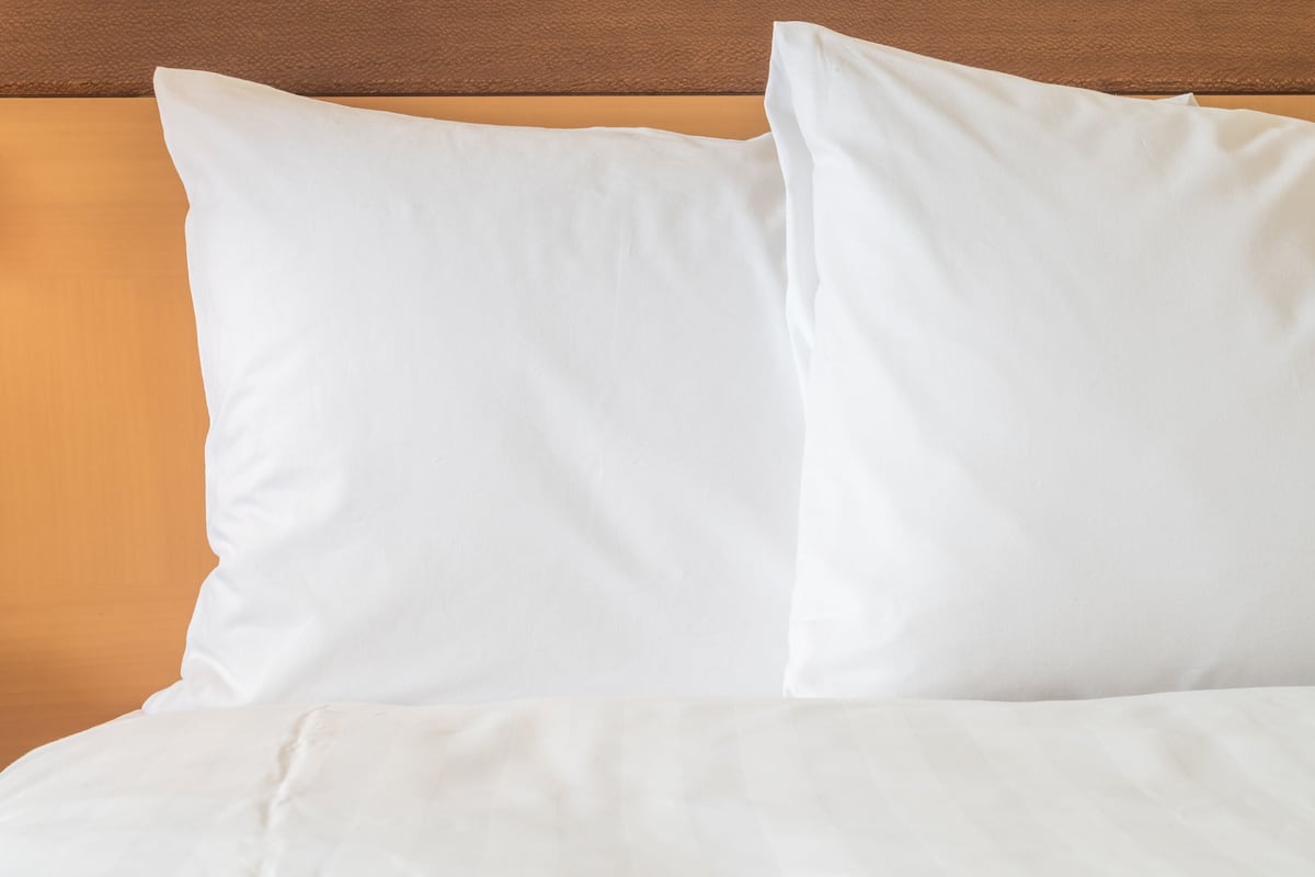 A bed with white bedding and pillows against a wooden headboard.