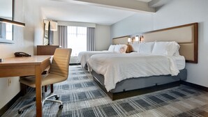 A hotel room with a desk, two beds, a chair, and a large mirror.