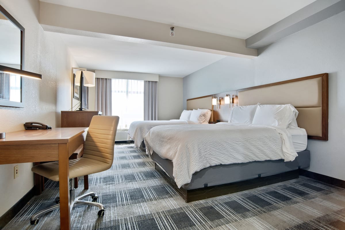 A hotel room with a desk, two beds, a chair, and a large mirror.