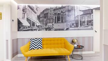 A yellow sofa with a chevron pillow in a modern room with a large black and white photograph on the wall.