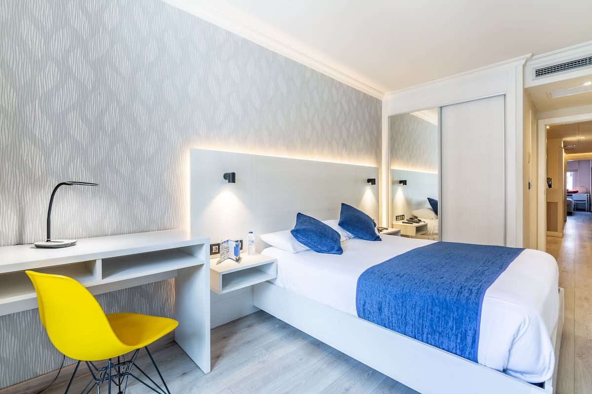 Ein modernes Hotelzimmer mit Bett, Schreibtisch, Stuhl und Spiegel.