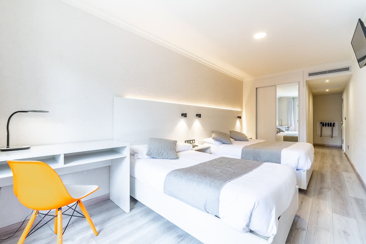 Ein modernes Hotelzimmer mit zwei Betten, einem Schreibtisch und einem leuchtend orangefarbenen Sessel.