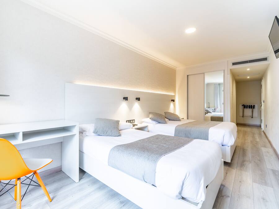 A hotel room with two beds, a desk, a chair, and a mirror.