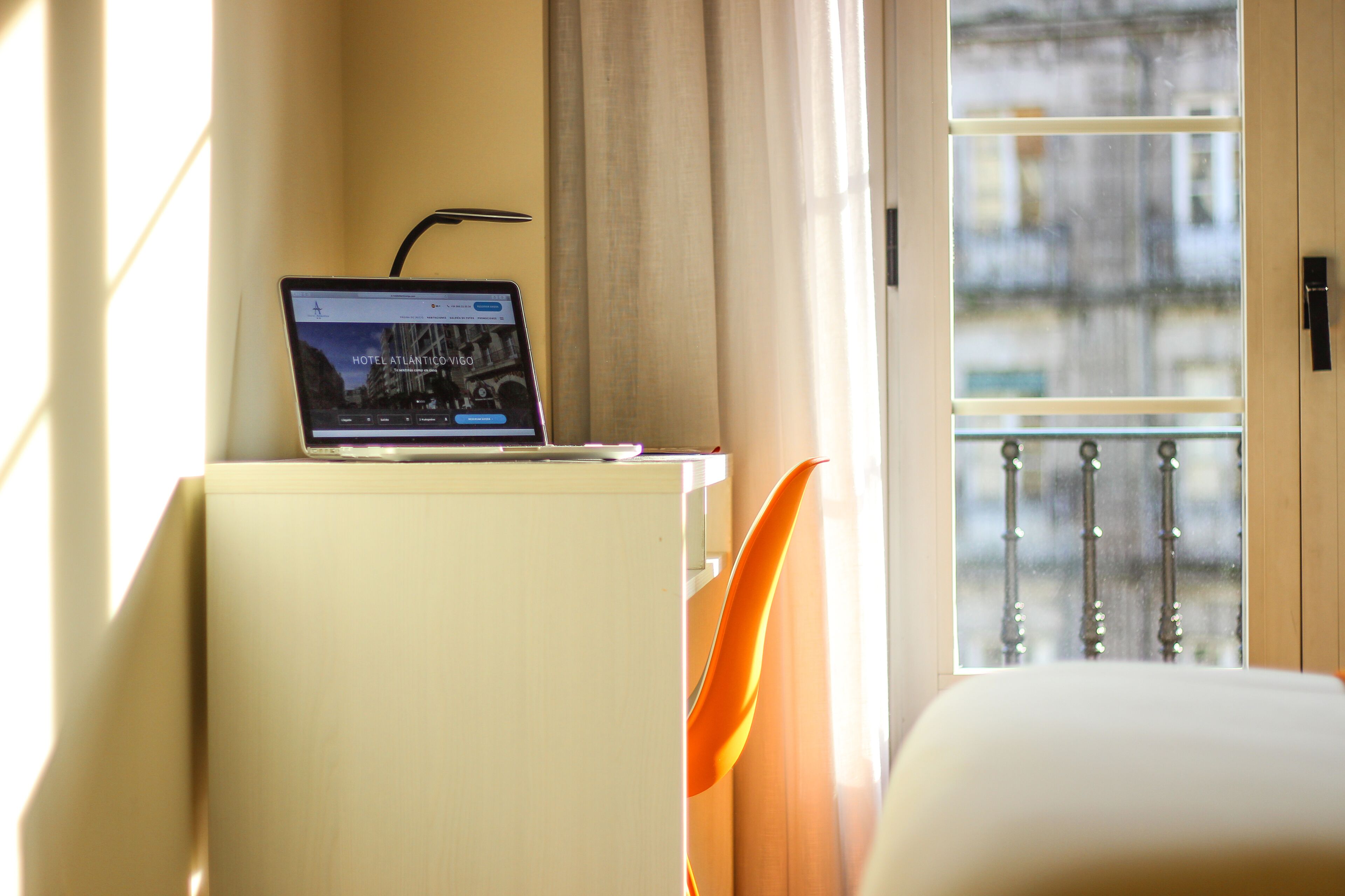 A laptop on a desk with a view of a balcony and a window.